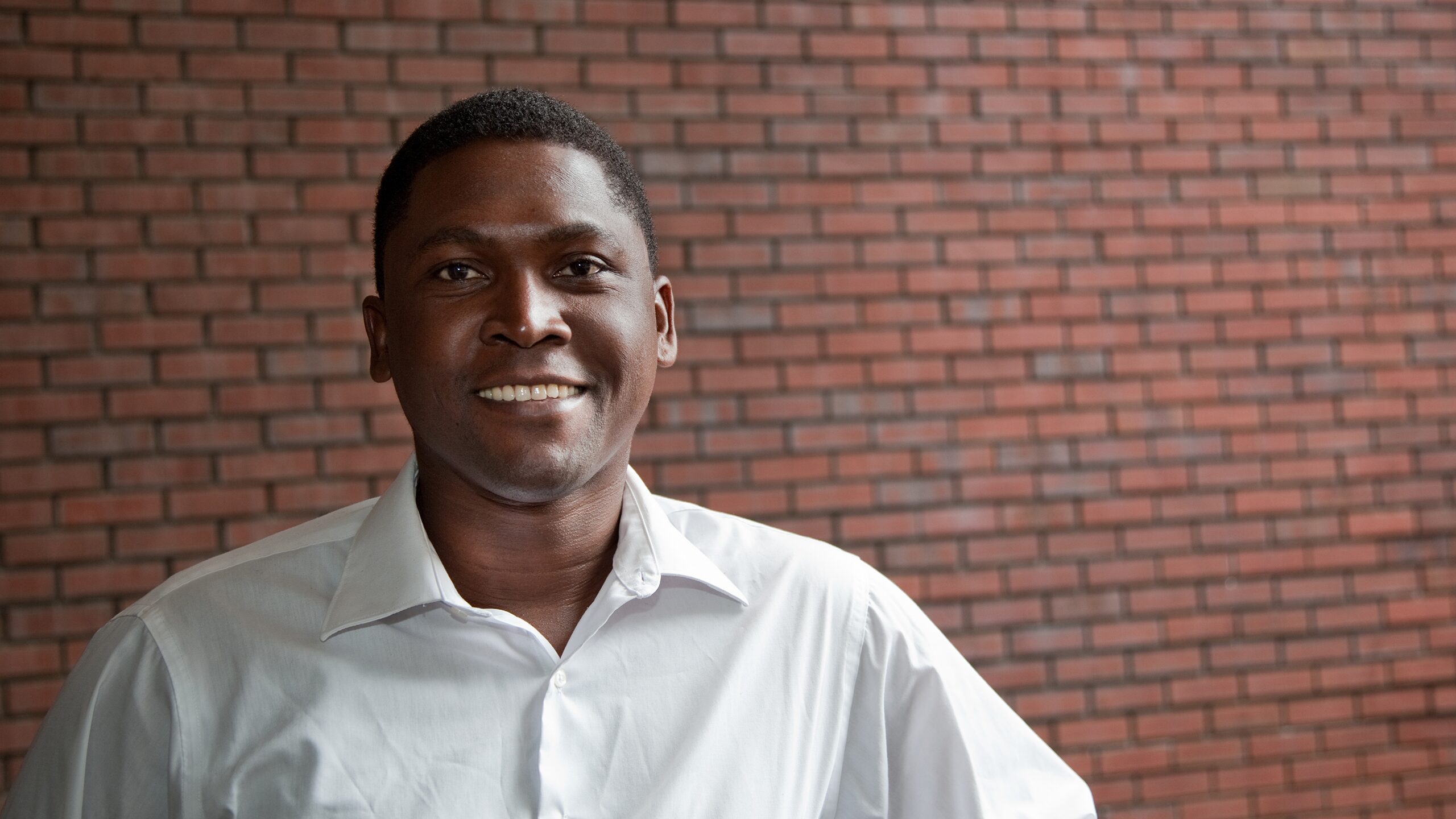 Smiling man standing in front of a brick wall.